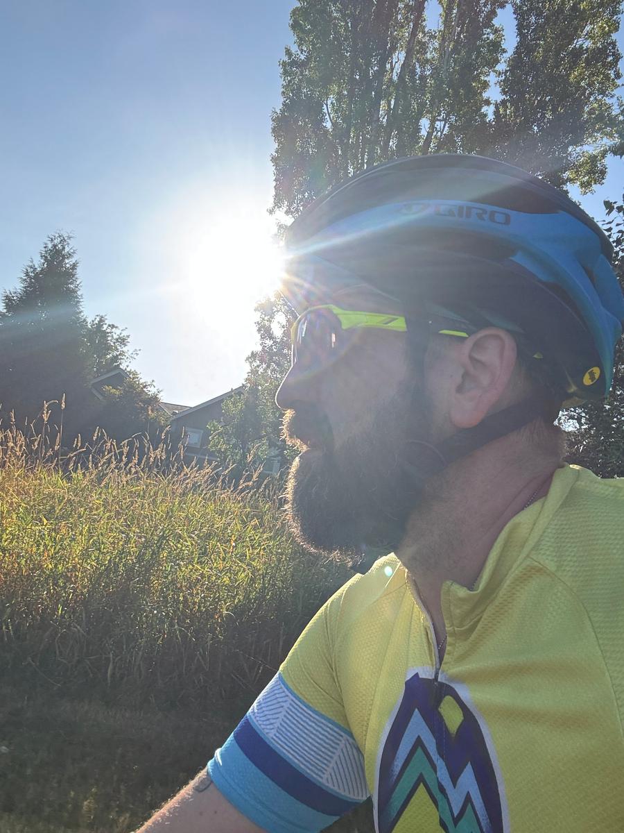 Matt Lyman in a yellow cycling jersey and blue helmet, riding into low sun