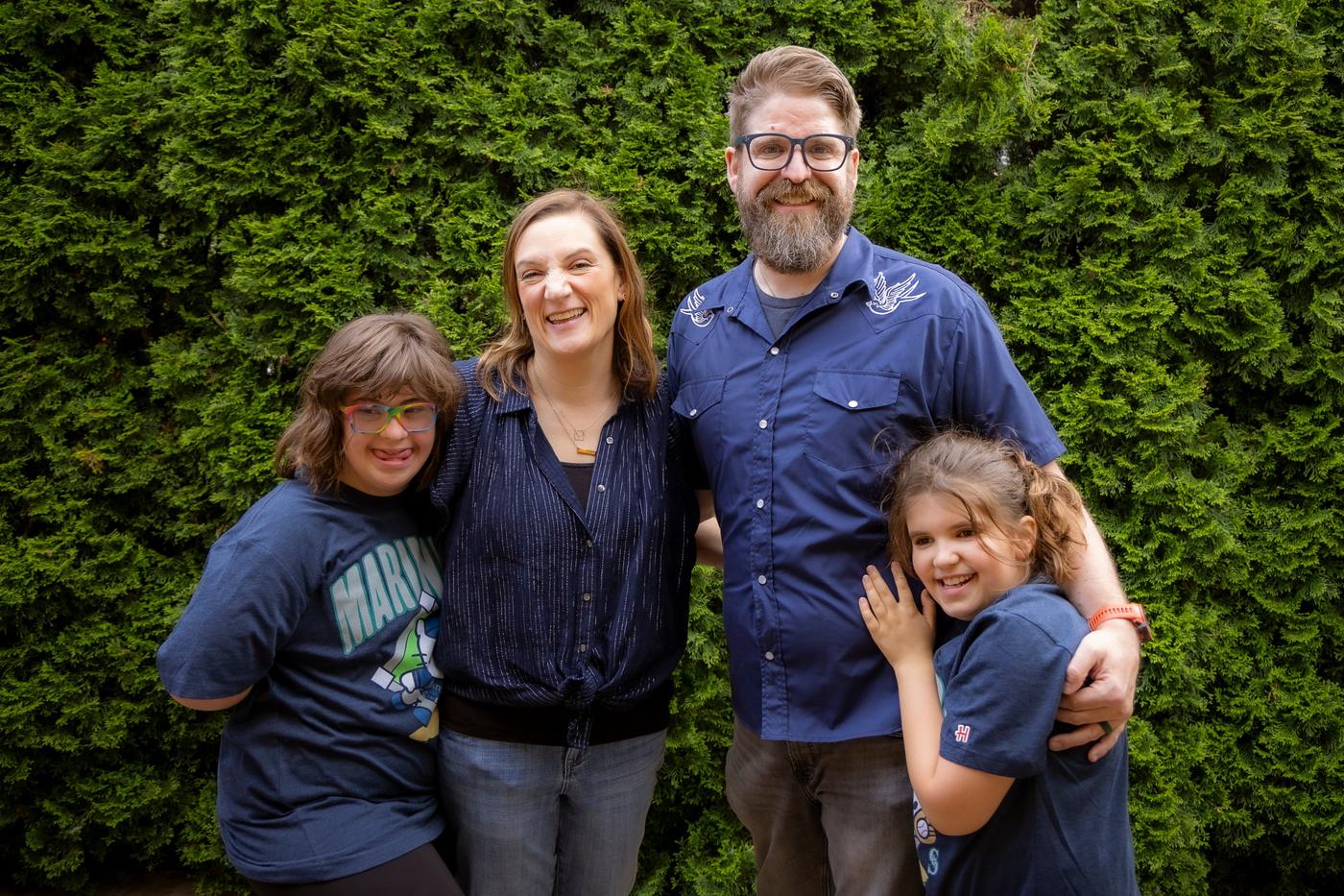 Matt Lyman with his family, smiling and arm in arm in front of a tall green hedge