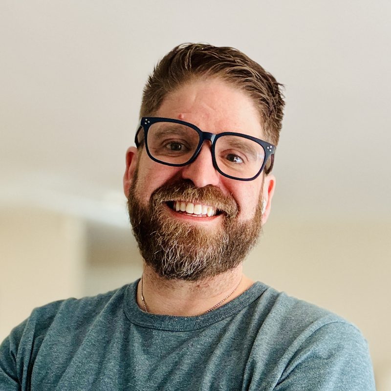 Matt Lyman smiling, wearing dark-framed glasses and a gray-blue t-shirt